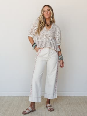 An all-cream boho look with a lace eyelet peplum top and wide-leg embroidered pants, styled with stacked beaded bracelets and flat sandals — effortless and warm, like a summer morning that went exactly right.