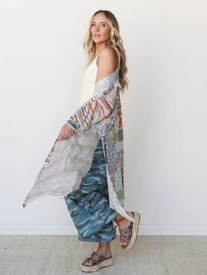 A layered boho outfit built around a patchwork duster worn open over a cream textured tank and wide-leg camo pants, styled with stacked turquoise bracelets and espadrille platform sandals — the kind of mix-everything look that somehow just works.
