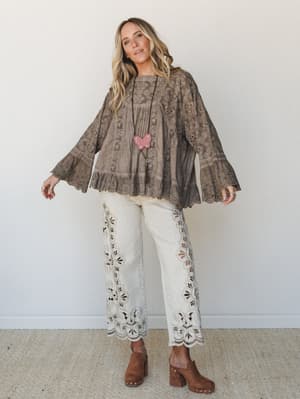 A breezy, textured two-piece set in washed taupe — an oversized eyelet top with dramatic bell sleeves paired with cream wide-leg pants detailed in floral cutwork embroidery, styled with suede platform clogs and a butterfly pendant necklace for a full