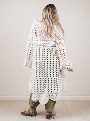 Person wearing a long, white crochet dress with a neutral background