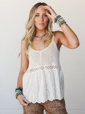 A white crochet-knit camisole top with eyelet trim and a flowy woven hem worn over leopard print pants, styled with layers of beaded bracelets and a turquoise pendant necklace — the kind of outfit that feels intentional without trying too hard.