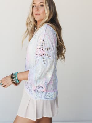 A dreamy pastel crochet shrug layered over a cream mini skirt — soft, handcrafted, and styled with stacked turquoise and beaded bracelets that feel like they came home from a beach trip and never left.