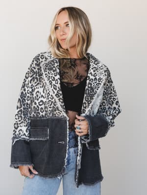 A mixed-media oversized blazer combining leopard print woven fabric on top with washed black denim on the bottom half, styled open over a black lace top and light blue jeans — the kind of piece that looks like it came from a really good vintage find.