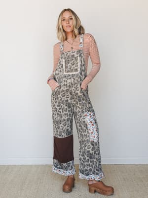 A wide-leg leopard print overall with patchwork floral and colorblock panels is layered over a rust stripe long-sleeve top and finished with tan clogs — the kind of outfit that looks like it came together effortlessly but definitely didn't.