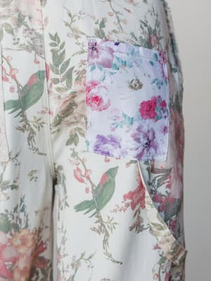 A close-up detail shot of a cream floral jumpsuit, highlighting a contrast chest pocket in a coordinating but distinctly different floral print — soft botanical meets bold blooms, and somehow it works perfectly.