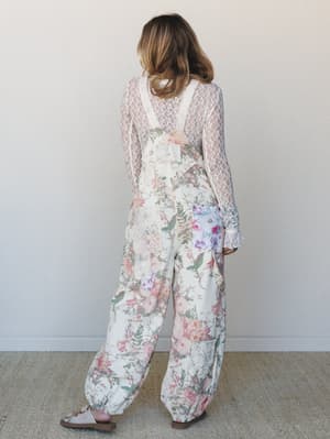 Shot from the back, a model wears a wide-leg floral jumpsuit layered over a sheer lace long-sleeve top — the kind of outfit that looks like it came together effortlessly but was absolutely thought through.
