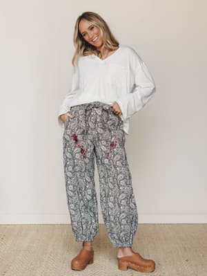 A relaxed, lived-in outfit pairing oversized white long-sleeve top with paisley-print jogger pants and tan wooden clogs — the kind of look that feels effortless on a slow morning but put-together enough to actually go somewhere.