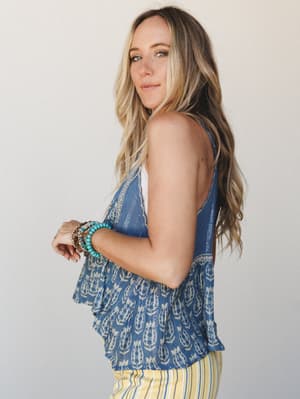 A side-profile shot of a model in a flowy indigo printed tank top with delicate lace trim, paired with yellow stripe pants and stacked turquoise bracelets — effortless and sun-warmed, like the start of a really good summer day.