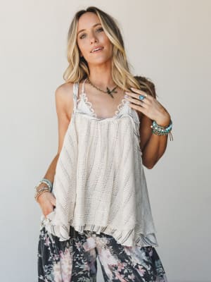 A flowy, open-knit cami top in natural cream is styled with dark floral wide-leg pants — the kind of effortless boho pairing that looks like it came together on a good day, not a planned one.