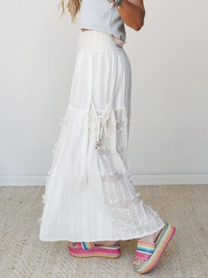 A flowy white wide-leg pant with tiered lace and fringe detailing is styled with a cropped grey tee and rainbow platform espadrilles — effortlessly boho with just enough whimsy.