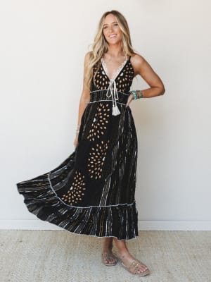 A flowy black maxi dress with a mixed print — dotted bursts and vertical stripe detail — styled with turquoise stacked bracelets and nude sandals, giving off that effortless boho energy you'd wear to a summer dinner and still feel like yourself.