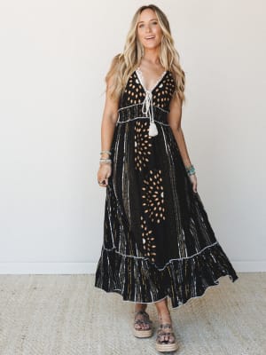 A black multi-print maxi dress with eyelet cutout details and tassel tie front, styled with platform espadrille sandals and stacked bracelets — boho and grounded at the same time.