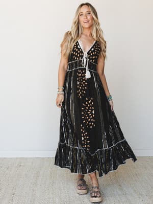A black multi-print maxi dress with eyelet cutout details and tassel tie front, styled with platform espadrille sandals and stacked bracelets — boho and grounded at the same time.