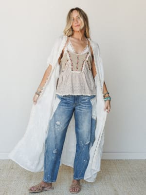 A layered boho look built around a floor-length white lace kimono worn open over an embroidered cami top and relaxed distressed jeans — the kind of outfit that looks effortless but was definitely thought about.