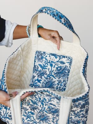 A close-up of the interior of a quilted block-print tote bag held open by two hands — cream quilted lining, a floral interior pocket, and a striking blue-and-ivory botanical print on the outside make this feel like the bag that goes everywhere withou