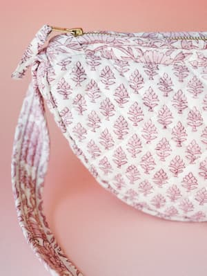 A close-up of a quilted fabric bag in ivory and dusty mauve, covered in a repeating block-print botanical motif — the kind of bag that looks like it wandered out of a vintage Indian textile market in the best possible way.