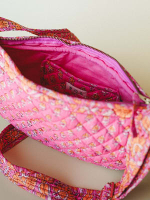 An open quilted crossbody bag in a vibrant pink and orange block-print floral, shot close-up to show off the roomy interior, interior pocket, and that satisfying diamond-quilted lining — the kind of bag that makes you actually want to stay organized.