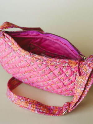 A quilted cotton crossbody bag in bright pink with an allover block-print floral pattern sits open against a neutral backdrop, showing off its magenta fabric interior and gold zipper hardware.