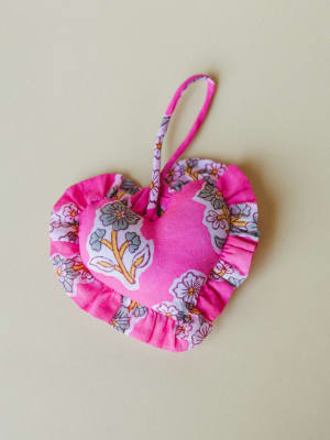 A stuffed fabric heart ornament in fuchsia and floral print, trimmed with gathered ruffle edges and a hanging loop — the kind of little thing you'd hang somewhere just to make yourself smile.