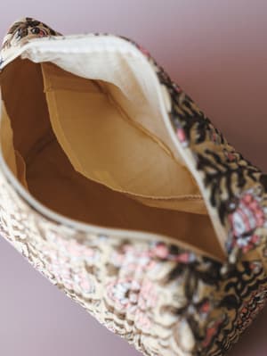 A close-up detail shot of a woven fabric bag shot open to reveal its camel-toned interior lining, with a mixed floral and abstract print visible on the exterior — earthy, textured, and quietly expressive.