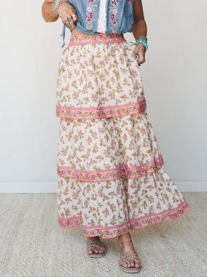 A tiered floral maxi skirt in cream with pink and yellow rosebud print, styled with a knotted chambray embroidered top and stacked jewelry — the kind of outfit that feels like a farmers market and a slow Saturday morning at the same time.