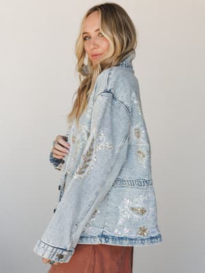 A light wash denim jacket covered in intricate floral and paisley beading and sequin embroidery — the kind of piece that does all the talking while you just stand there looking like you meant to.