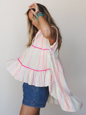 A breezy tiered tank top in ivory with multicolor wavy stripes catches mid-twirl, styled with denim shorts and a stack of turquoise bracelets — the kind of top that makes a Tuesday feel like vacation.