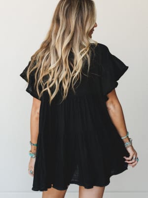 A breezy black mini dress shot from the back, with ruffle sleeves and a flowy babydoll silhouette — styled with stacks of turquoise and silver boho jewelry that do all the talking.