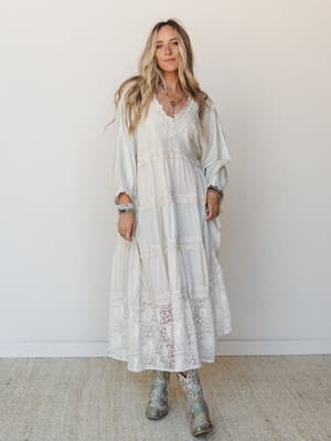 A flowy tiered maxi dress in soft sage and cream with wide lace panels throughout, styled with embroidered cowboy boots and layered boho jewelry — the kind of dress that makes you feel like you wandered into a garden party and never left.