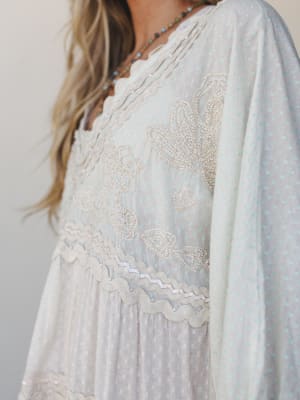 A dreamy close-up of a flowy polka dot dress with intricate beaded butterfly appliqué and ric-rac trim detailing — the kind of piece that feels like it belongs at a garden party or a slow morning somewhere beautiful.