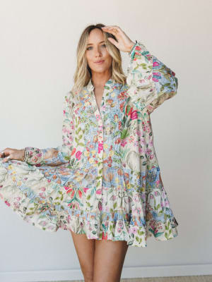 A flowy mixed-floral mini dress with long bishop sleeves and a tiered ruffle hem — the kind of dress that looks like a garden party and a good mood all at once.