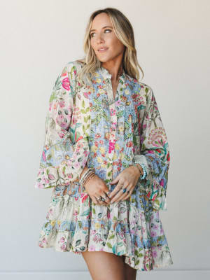 A mixed floral patchwork mini dress in cream and soft blue with wide bell sleeves and a tiered ruffle hem — the kind of dress that makes a Tuesday feel like something worth remembering.