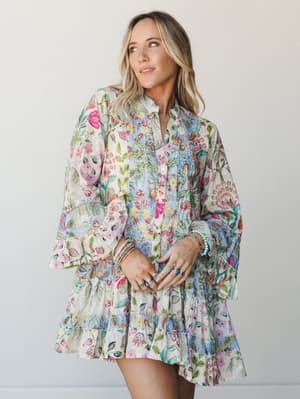 A mixed floral patchwork mini dress in cream and soft blue with wide bell sleeves and a tiered ruffle hem — the kind of dress that makes a Tuesday feel like something worth remembering.