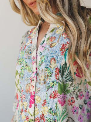 A close-up detail shot of a floral-printed button-front top or dress layered with dense bead and sequin embellishment along the placket and panels — the kind of piece that stops people mid-sentence.