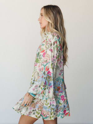 A flowy mini dress in a vivid mixed floral print comes alive from the side — long sleeves, tiered ruffle hem, and a garden's worth of color make it feel like something you'd wear to wander a farmers market and never want to take off.