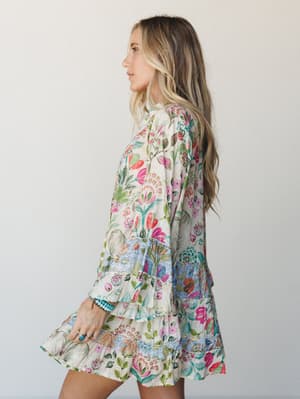 A flowy mini dress in a vivid mixed floral print comes alive from the side — long sleeves, tiered ruffle hem, and a garden's worth of color make it feel like something you'd wear to wander a farmers market and never want to take off.
