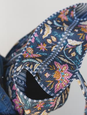 A close-up detail shot of a quilted tote bag in a rich navy floral print, showing an open interior zipper pocket — the kind of bag that makes you actually want to be organized.