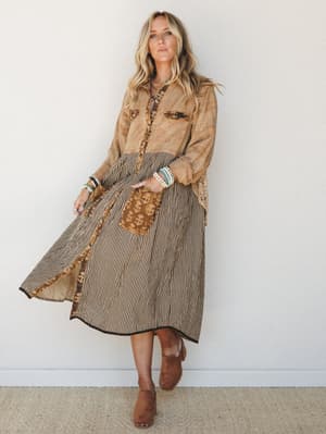 A mixed-print midi dress with a button-front bodice in a washed camel textile and a flowing striped skirt, styled with stacked bracelets, layered necklaces, and suede clogs — earthy, effortless, and deeply personal.