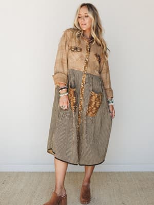 A relaxed, patchwork midi dress in warm mocha tones worn with stacked boho jewelry and suede mules — the kind of piece that looks like it was thrifted in the best possible way.