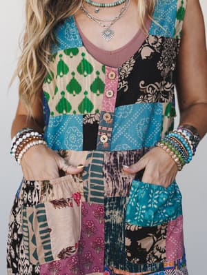 A close-up torso shot of a patchwork sleeveless jumpsuit layered over a dusty rose tank, styled with stacked bracelets, layered silver necklaces, and a turquoise beaded necklace — the kind of outfit that looks like it was assembled with intention and