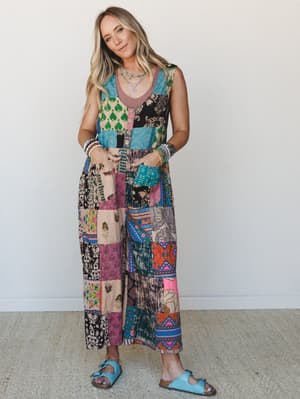A patchwork maxi jumpsuit in a kaleidoscope of mixed prints and colors worn with turquoise sandals and layered boho jewelry — the kind of outfit that makes people stop and ask where you got it.