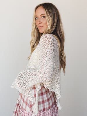 A cream open-weave crochet poncho layered over a dusty rose plaid skirt — the kind of effortless, soft pairing that looks like it came together without trying but absolutely did not.