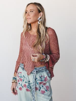 A relaxed, layered look built around a dusty rose open-knit poncho top paired with soft mint floral embroidered pants — the kind of outfit that feels equally at home at a weekend market or a breezy dinner out.