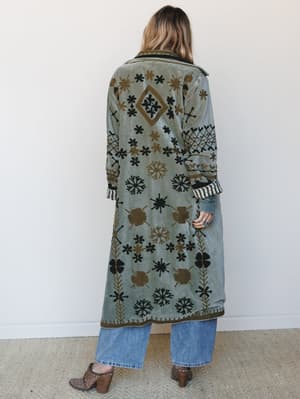 Shot from the back, this maxi-length velvet duster coat is covered in intricate floral and botanical embroidery in black and golden olive — the kind of piece that makes people stop you on the street to ask where you got it.