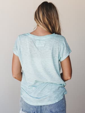 A back-view shot of a relaxed aqua burnout tee with rolled short sleeves, paired with embroidered denim shorts — easy, lived-in, and just the right amount of effortless.