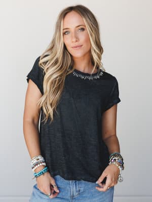 A relaxed acid-wash black tee with embroidered neckline detail, styled with stacked beaded bracelets and light-wash denim — the kind of effortless everyday look that somehow always gets compliments.