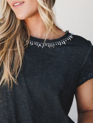 A worn-in black tee with a sweet boho twist — delicate embroidered stitching along the neckline gives it just enough personality to make a simple top feel like a whole outfit.