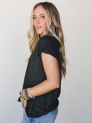 A relaxed side-profile shot of a model in a soft black tee and light-wash jeans, her wrist stacked with colorful beaded bracelets doing most of the talking — effortless and a little personal.