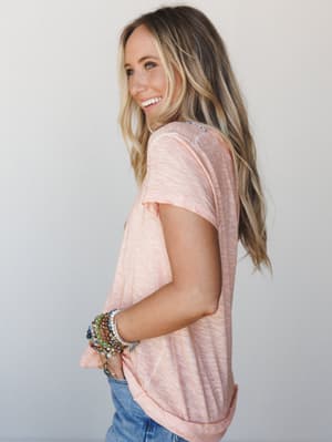 A side-profile shot of a model in a relaxed coral peach slub tee, stacked with colorful beaded bracelets and a hint of denim — the kind of easy, happy outfit you'd throw on without thinking twice.
