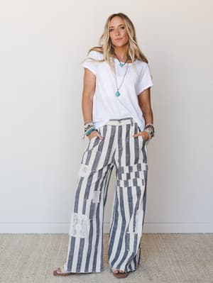 A relaxed, sun-warmed look built around wide-leg striped pants with lace patchwork details, paired with a simple white tee and layered turquoise jewelry — the kind of outfit that feels effortless but totally intentional.